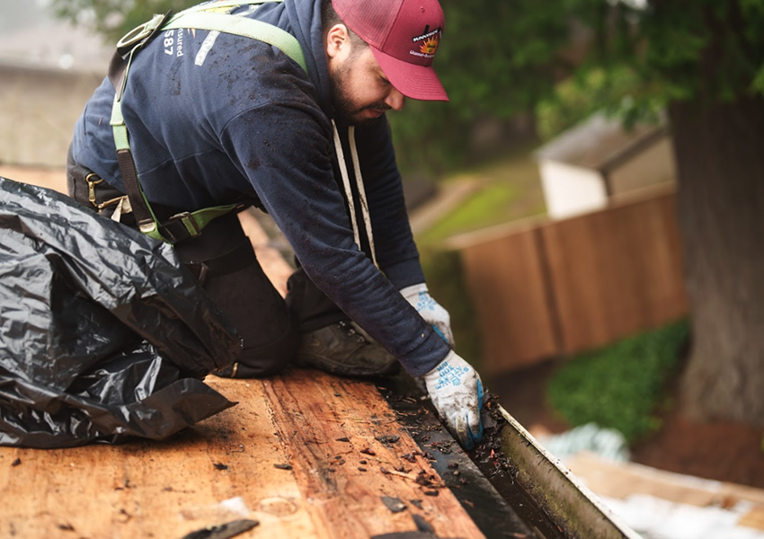 Sunnyside Roofing worker cleaning gutters into a trash bag